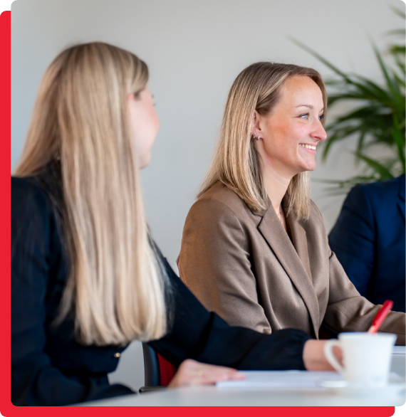 bau-immobilien-expansion-img-2 Das Bild zeigt zwei Frauen in Business-Kleidung, die an einem Tisch sitzen. Eine der Frauen lächelt, während sie mit der anderen spricht. Auf dem Tisch steht eine Tasse.
